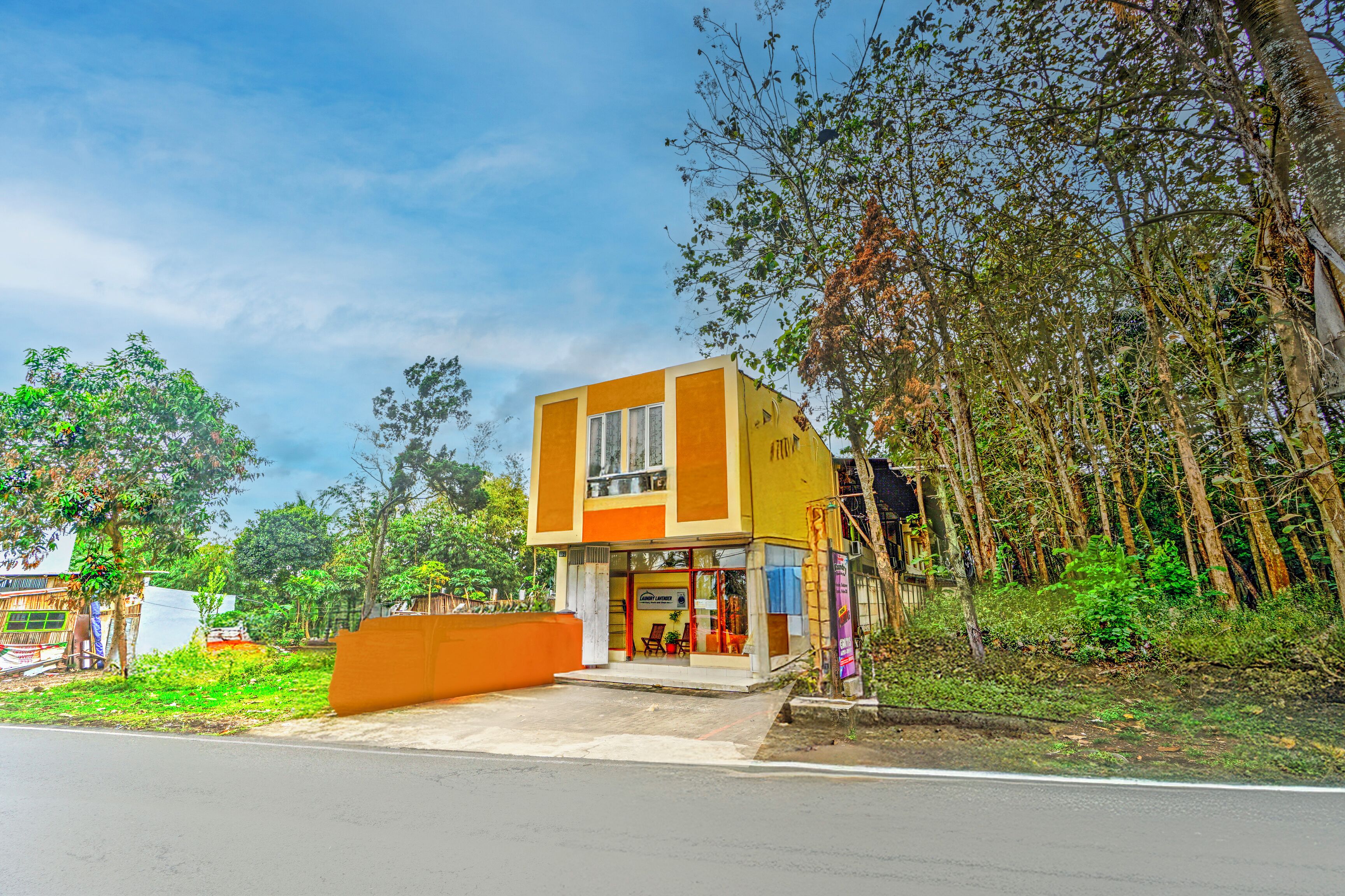 A two-story building with a yellow and orange facade, large windows, and a visible entrance with a small outdoor seating area.