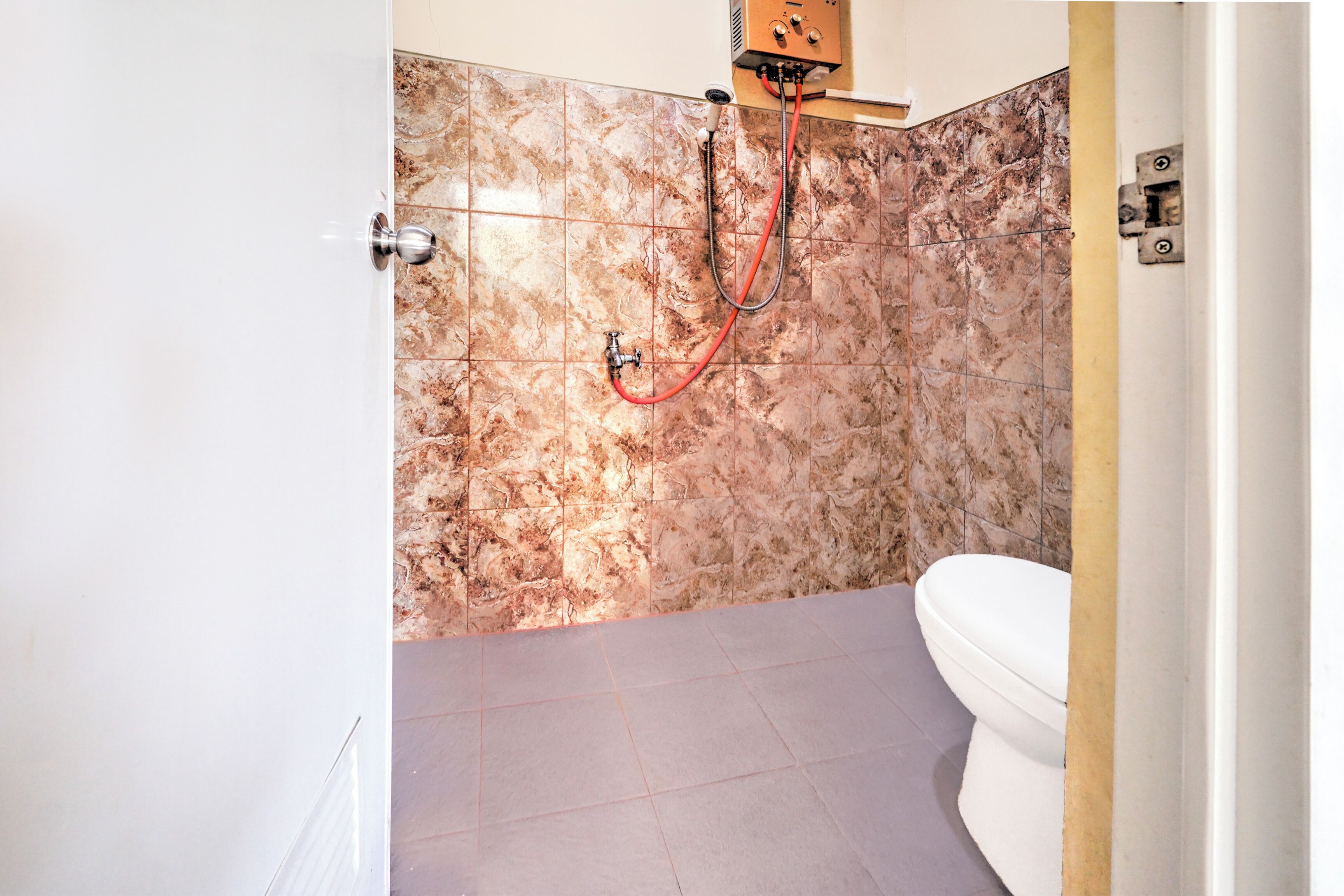 A bathroom with a shower, a toilet, and a marble-tiled wall.