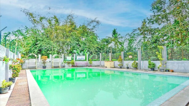 Una piscina rectangular con borde de azulejos, rodeada por un deck de concreto. Se observan plantas en macetas y una reja metálica al fondo.