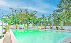 A rectangular swimming pool with a tiled edge, surrounded by a concrete deck. There are potted plants and a metal gate in the background. - Hotel O The Velodrome Inn near Exit Toll Malang (Jawa Timur)