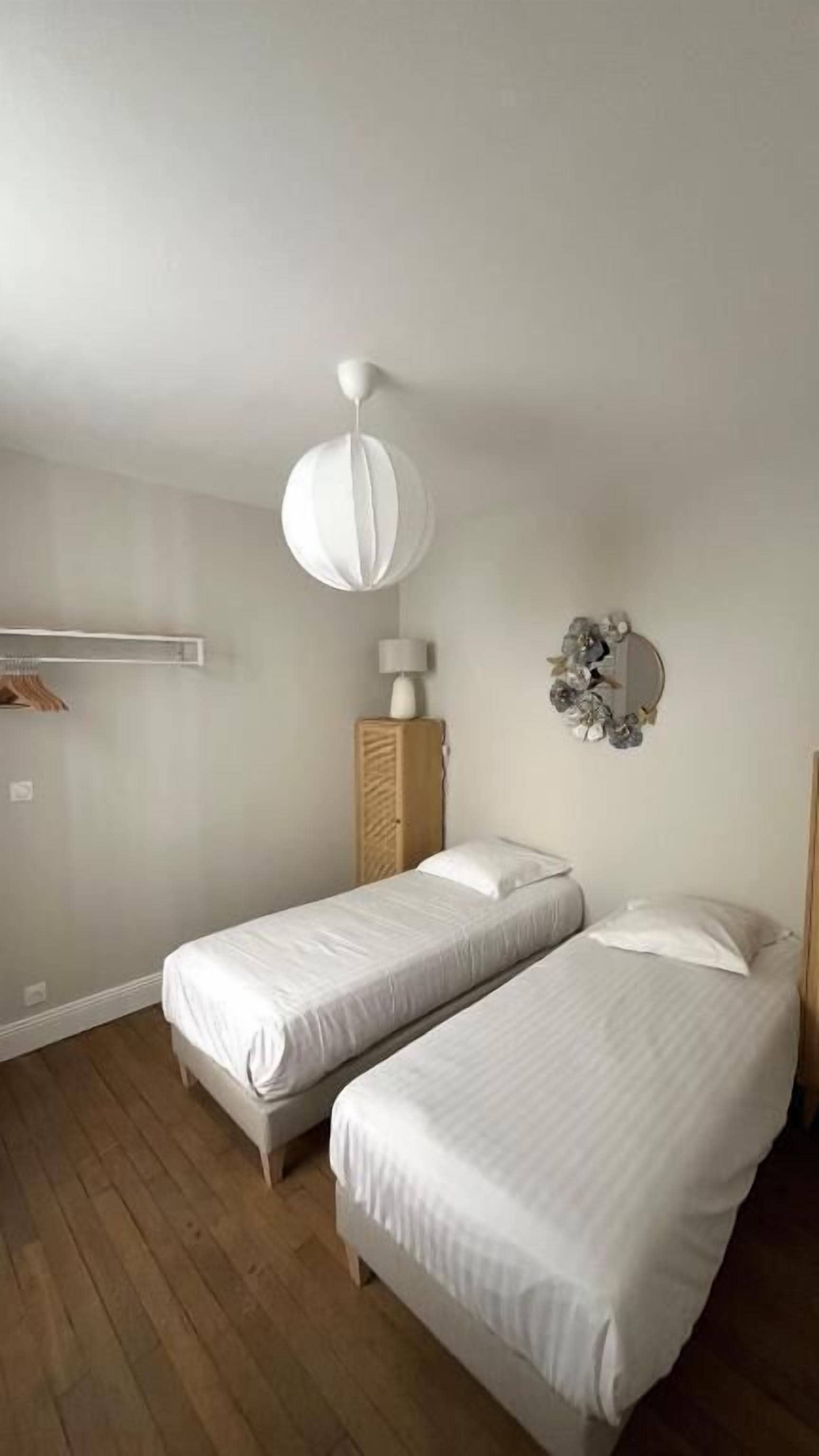 Een slaapkamer met twee eenpersoonsbedden, een houten kast, een hanglamp en een spiegel aan de muur.