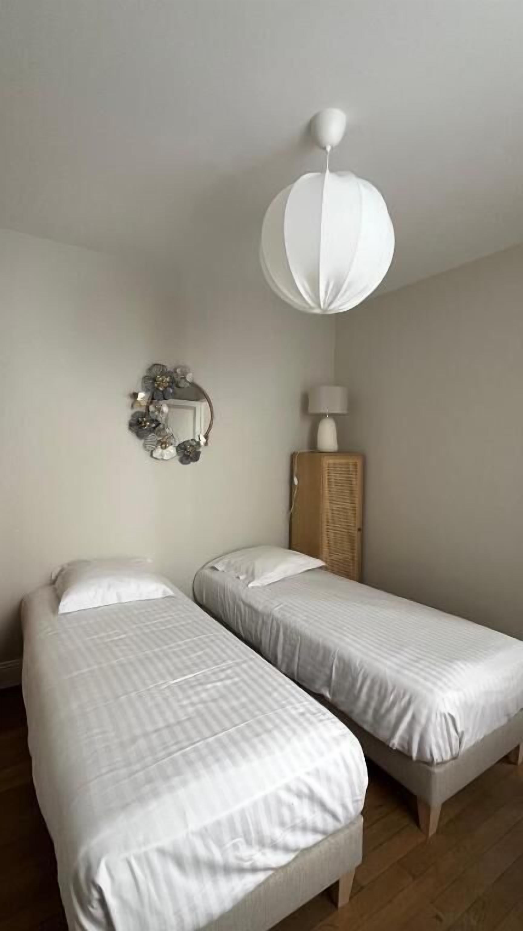 A room with two single beds, a wooden wardrobe, a wall-mounted mirror, and a hanging light fixture.