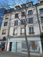 Un edificio con varias ventanas, un árbol en la parte delantera y un escaparate con un logo verde.