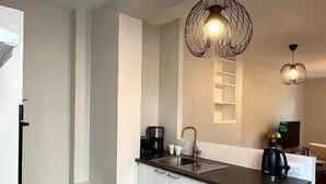 Une cuisine moderne avec des meubles blancs, un plan de travail noir et deux suspensions lumineuses.