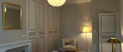 A bedroom with a large bed, a fireplace, a chair, and a lamp.