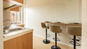 Une cuisine moderne avec un plan de travail en bois, un évier et une fenêtre. On y trouve trois tabourets de bar et une table à manger avec des assiettes et des verres.