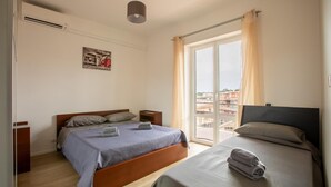 Une chambre avec deux lits, une fenêtre avec des rideaux, un ventilateur de plafond et un climatiseur fixé au mur.