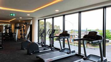 A gym with treadmills, weight machines, and a large window offering a view of the street.
