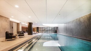 Una piscina interior moderna con vista despejada al área de la piscina, un espacio de descanso con sillas y una mesa, y un pilar grande.
