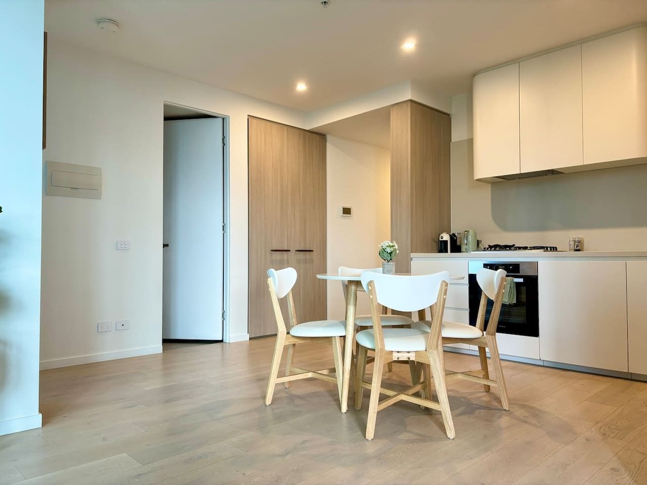 Een moderne keuken met witte kastjes, een eettafel met stoelen en een oven.