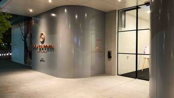 A modern building entrance with a curved facade, a glass door, and a sign indicating the name and number of the building.