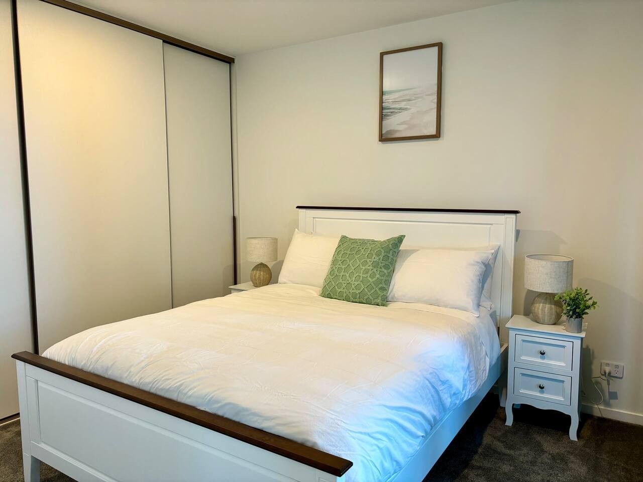 A bedroom with a bed, bedside tables, a nightstand, and a wall-mounted picture.
