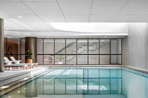 A modern indoor swimming pool with clear glass walls, a staircase leading to upper levels, and lounge chairs along the poolside. - SkyGarden Cozy Apt | Sunrise View · Pool · Parking (Glen Waverley)