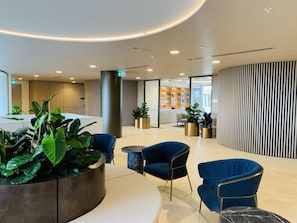 A modern lobby with seating areas, a reception desk, and a plant arrangement. - SkyGarden Cozy Apt | Sunrise View · Pool · Parking (Glen Waverley)