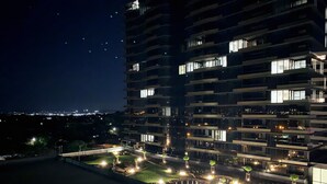 Un hotel de varios pisos con balcones iluminados y una zona ajardinada en la azotea con asientos y plantas.