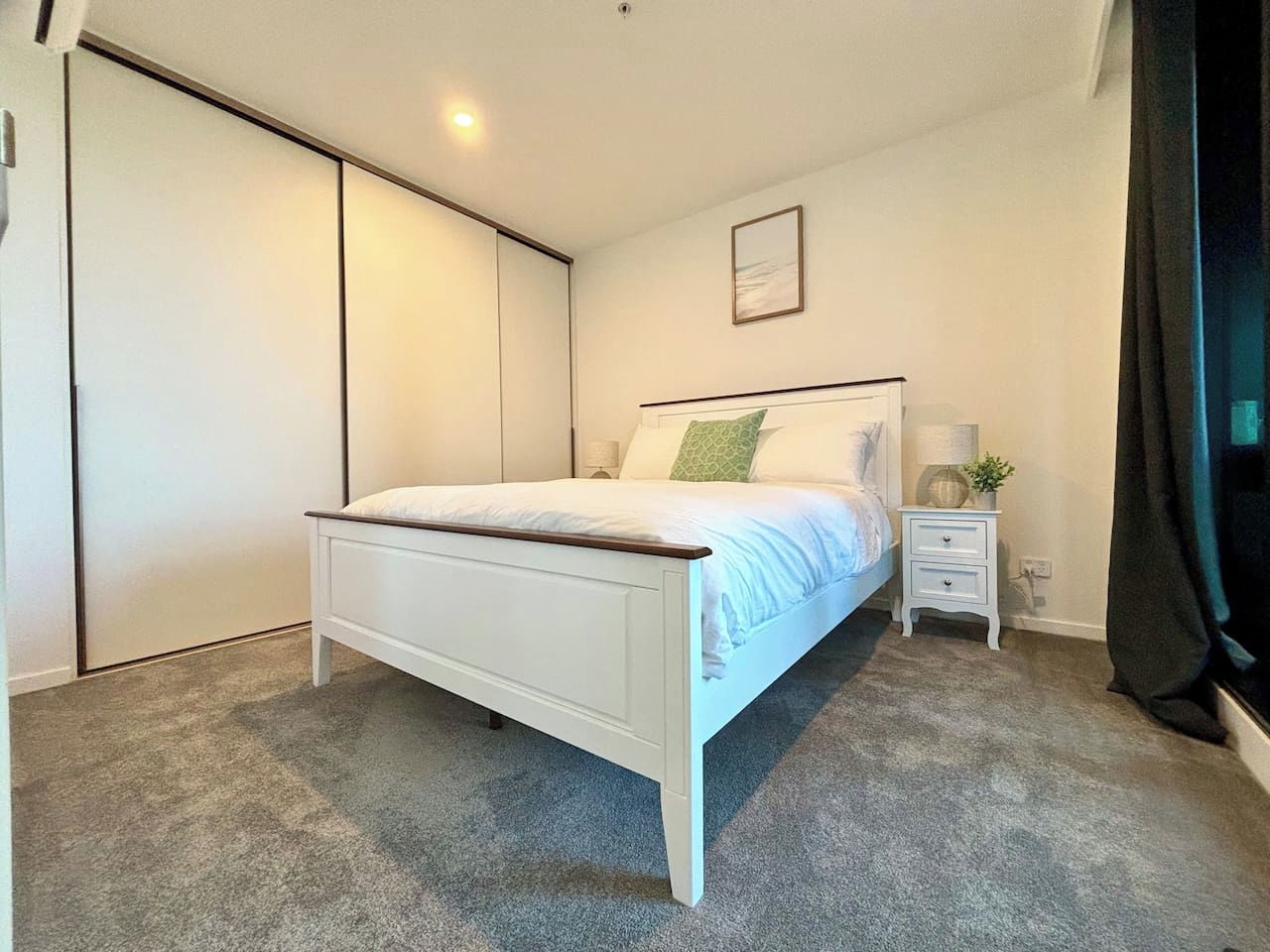 A bedroom with a bed, bedside table, lamp, and a wardrobe.