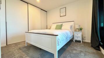 A bedroom with a bed, bedside table, lamp, and a wardrobe.