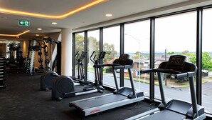Un gimnasio con cintas de correr, máquinas de pesas y vistas al exterior.