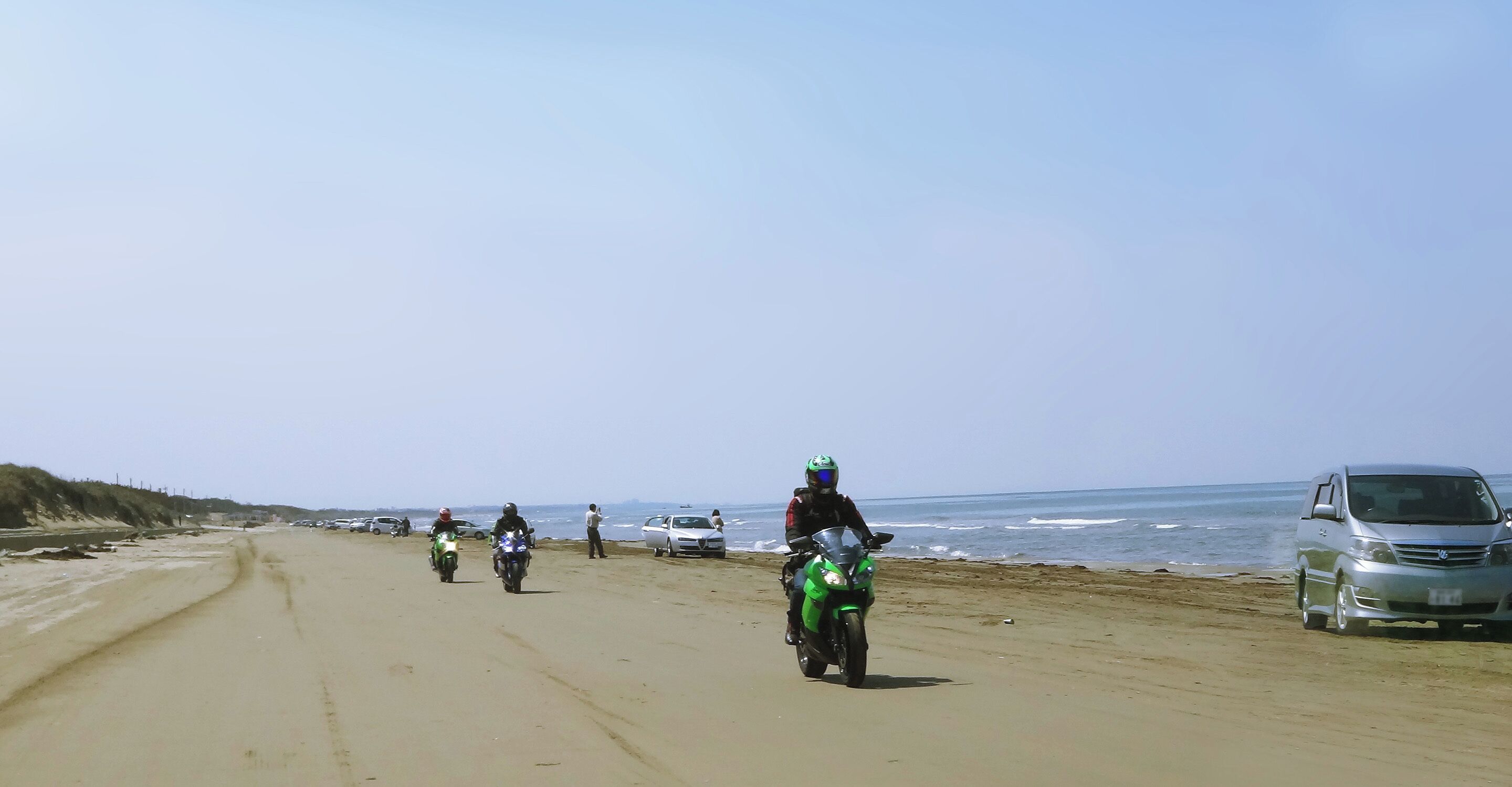 A beach with motorcycles and cars parked along the shore.