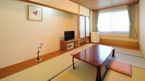 A traditional Japanese room with tatami flooring, a low wooden table, a television on a cabinet, and a window with curtains. - Hotel Wellness Notoji (Hodatsushimizu-cho)