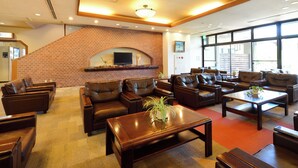 A hotel lobby with leather sofas, a brick fireplace, and large windows. - Hotel Wellness Notoji (Hodatsushimizu-cho)