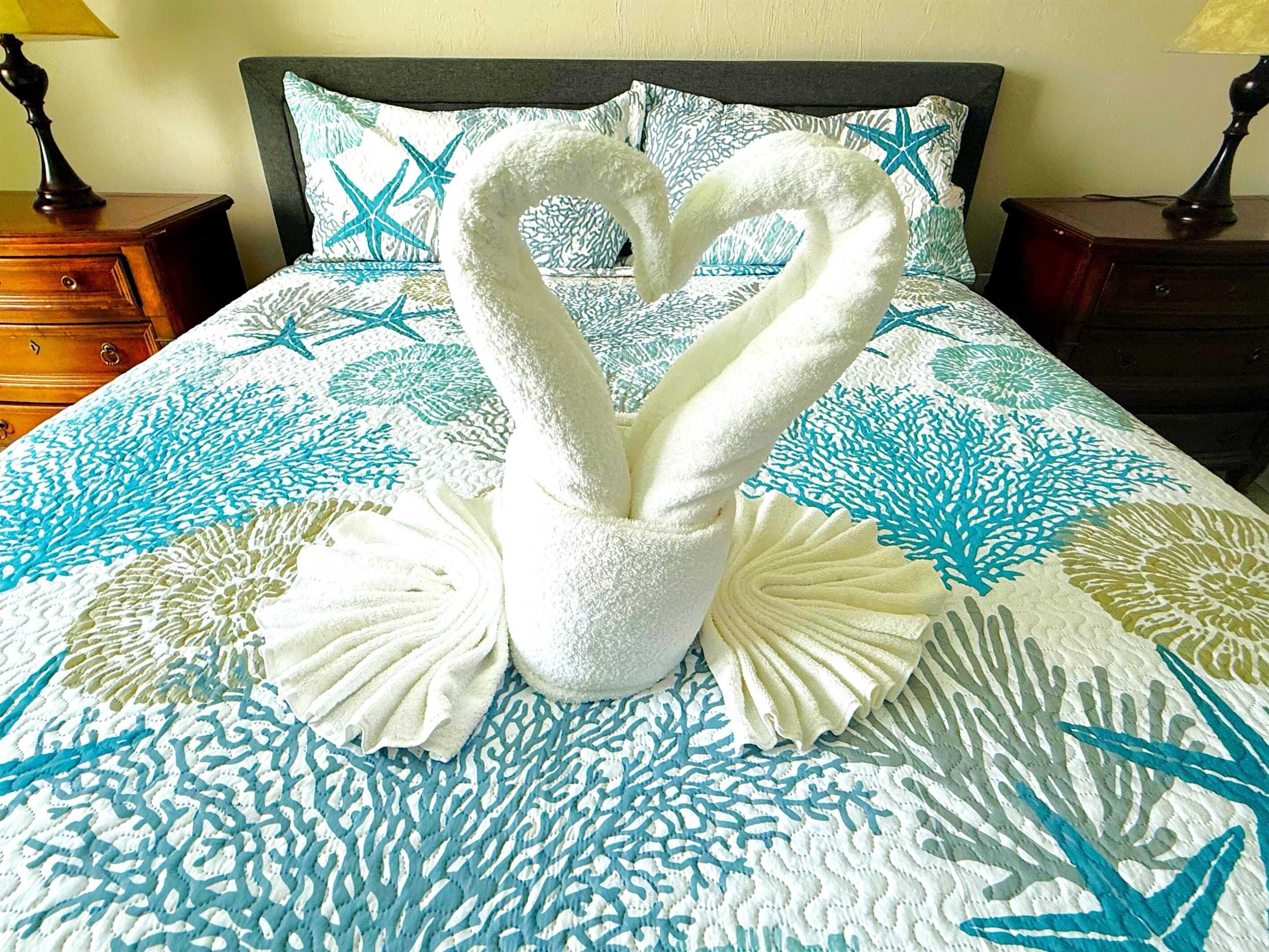 A bed with a decorative swan towel arrangement on a bedspread with a blue and white coral pattern.
