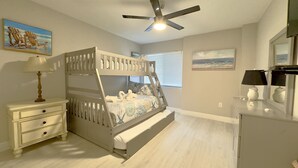 A bunk bed with a ladder, a bedside table with a lamp, a dresser, and a ceiling fan. - Island End Paradise - 2 Bedroom Beachfront (Fort Myers Beach)