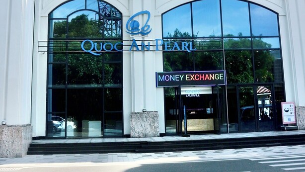 A building with a large glass facade, a Quoc Ak Pearl sign, and a Money Exchange sign. - Blue Waves Hotel (Phu Quoc)