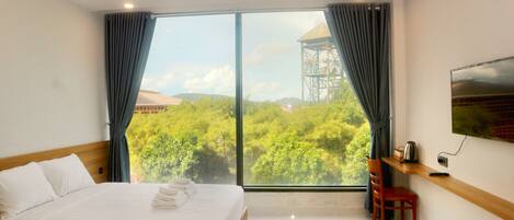 A hotel room with a large bed, a chair, a TV, and a view of a forest and a tower.