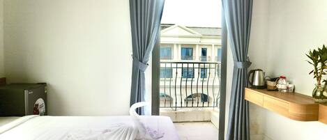 Habitación de hotel con cama, escritorio, silla y balcón con vista a un edificio.