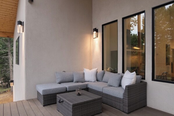 Un espace de détente extérieur moderne, comprenant un canapé d’angle, une petite table et des lampes fixées au mur.