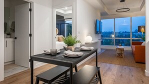 A modern dining area with a table set for two, a potted plant, and a view of the cityscape through large windows.
