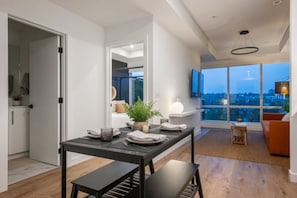 Uma sala de jantar moderna com uma mesa posta para dois, um vaso de planta e vista panorâmica da cidade através de amplas janelas.