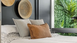 A bed with white and brown pillows, a grey headboard, and a window with a view of greenery.