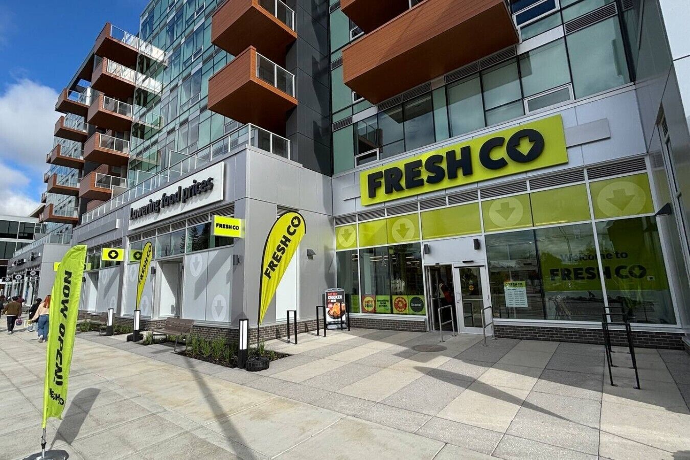 Moderni rakennus, jossa on FreshCo-niminen elintarvikeliike, ulkoilmaistumapaikkoja ja avoin, selkeä taivas.