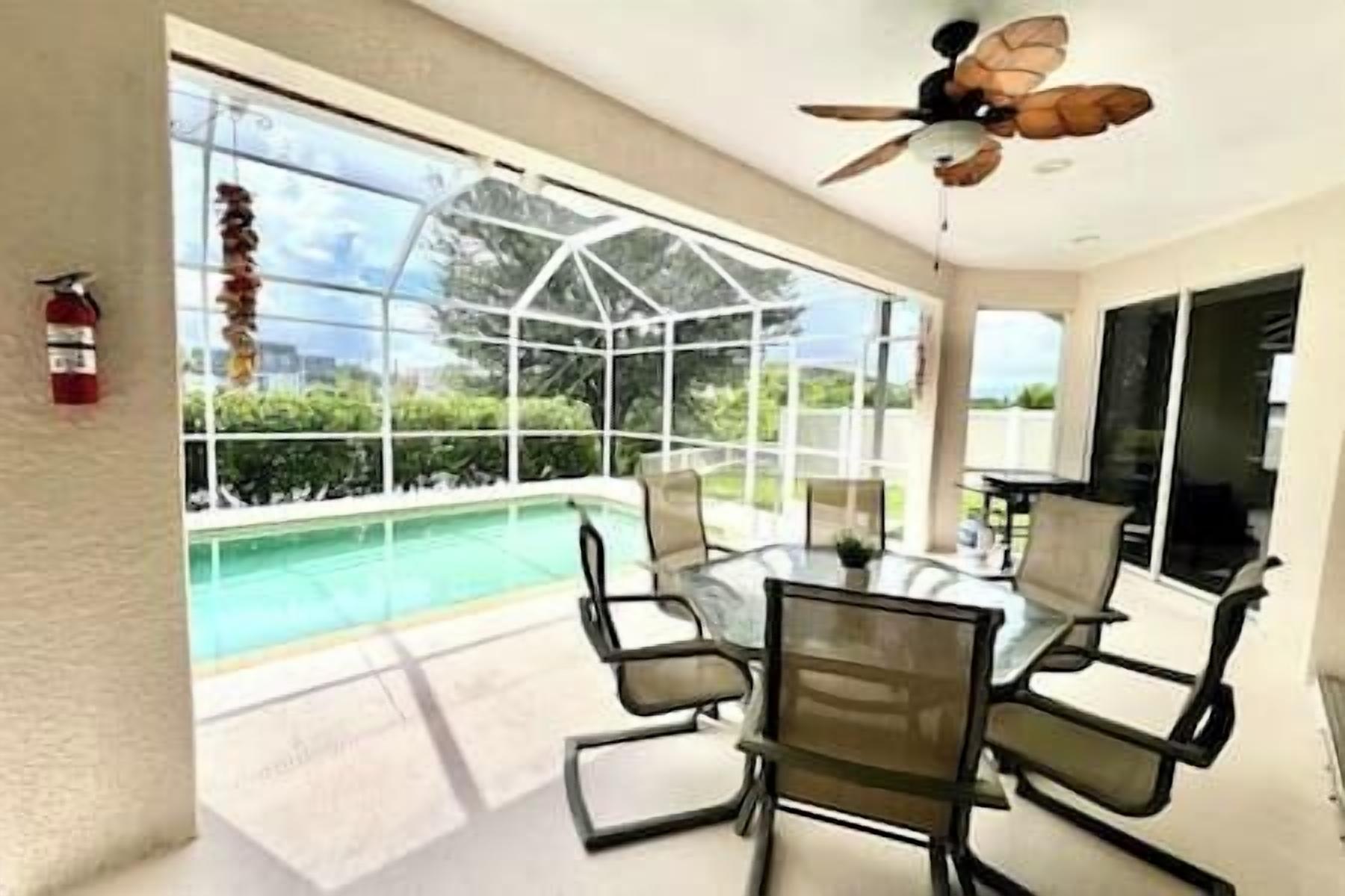 Un área junto a la piscina con cerramiento de vidrio, un ventilador de techo y una mesa con sillas.