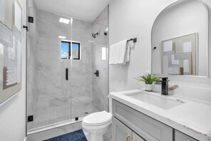 A modern bathroom with a glass-enclosed shower, a white toilet, a sink with a mirror, and a potted plant. - Casa Bella l Sleeps 10 l Near Freedom Park & MIA (Miami)