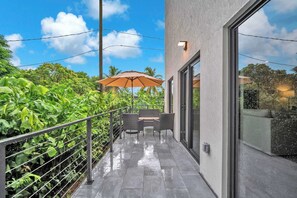 A modern outdoor patio with a metal railing, a table with chairs, and an umbrella. - Casa Bella l Sleeps 10 l Near Freedom Park & MIA (Miami)