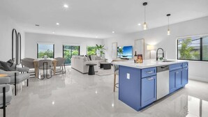 A modern kitchen with a blue island, white countertops, and a dining area with a gray sofa and chairs. - Casa Bella l Sleeps 10 l Near Freedom Park & MIA (Miami)