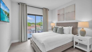 Une chambre d’hôtel moderne avec un grand lit, deux tables de chevet, une vue sur l’extérieur et des œuvres d’art accrochées aux murs.