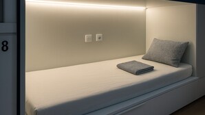 Quarto compacto e moderno com cama, travesseiro e mesa de cabeceira.