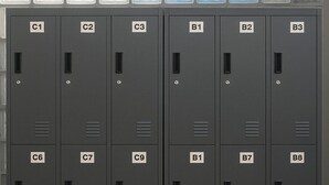 Uma fileira de armários metálicos cinzentos, com etiquetas de C1 a C9 e de B1 a B10.