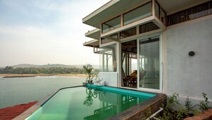 A modern house with a swimming pool, large windows, and a view of the water. - Amã Stays & Trails Athaang, Dapoli (Dapoli)