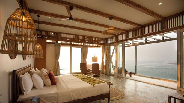 A spacious bedroom with a large bed, wooden beams, a view of the ocean, and a balcony. - Amã Stays & Trails Athaang, Dapoli (Dapoli)