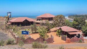 A coastal hotel with multiple red-roofed buildings, a signboard, and a view of the sea. - Amã Stays & Trails Athaang, Dapoli (Dapoli)