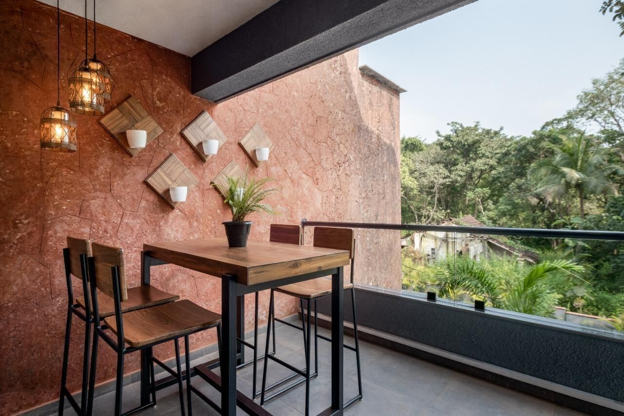A balcony with a wooden table and chairs, a potted plant, and hanging pendant lights.