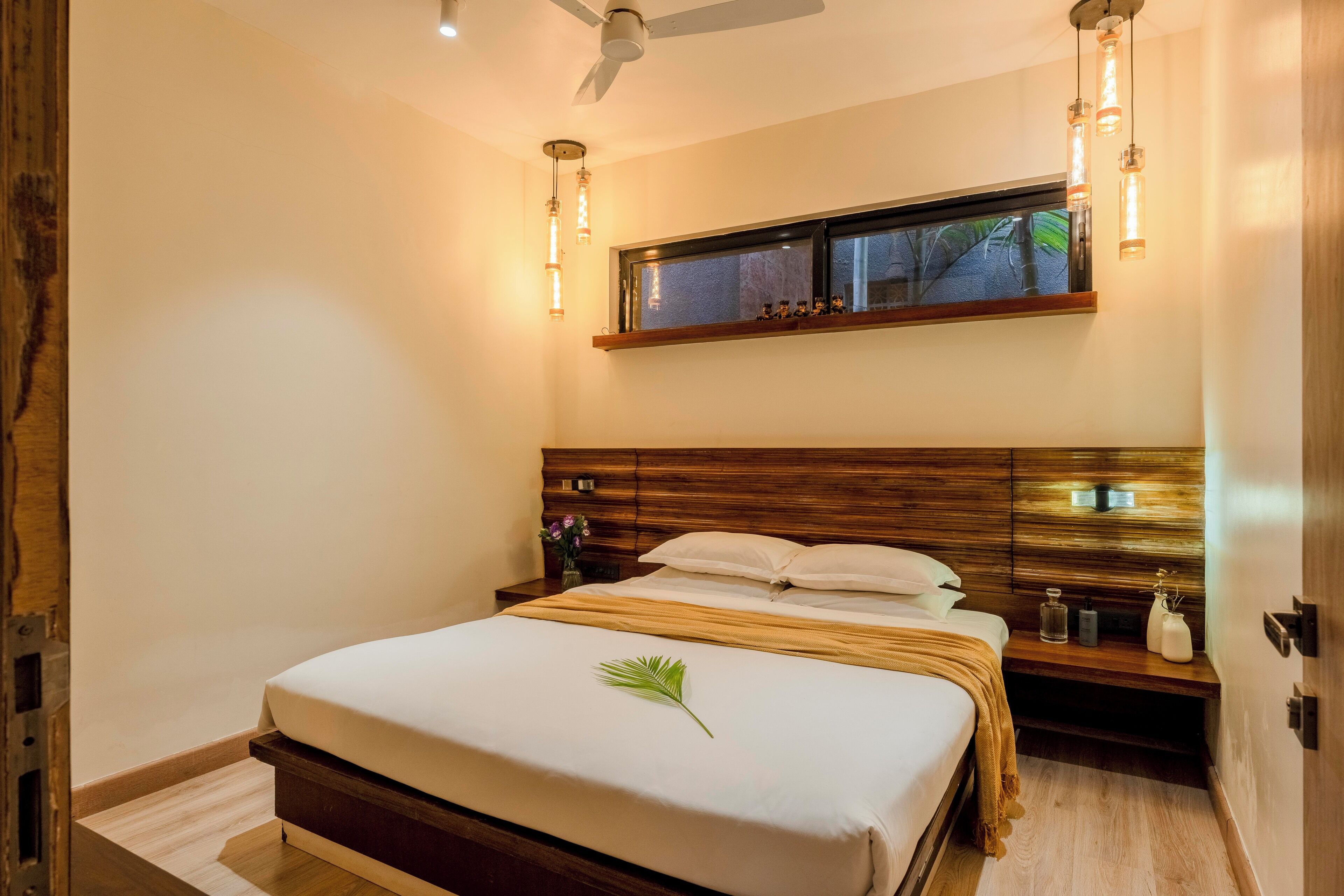 A bedroom with a large bed, wooden headboard, bedside tables, a window with a view, and pendant lighting.