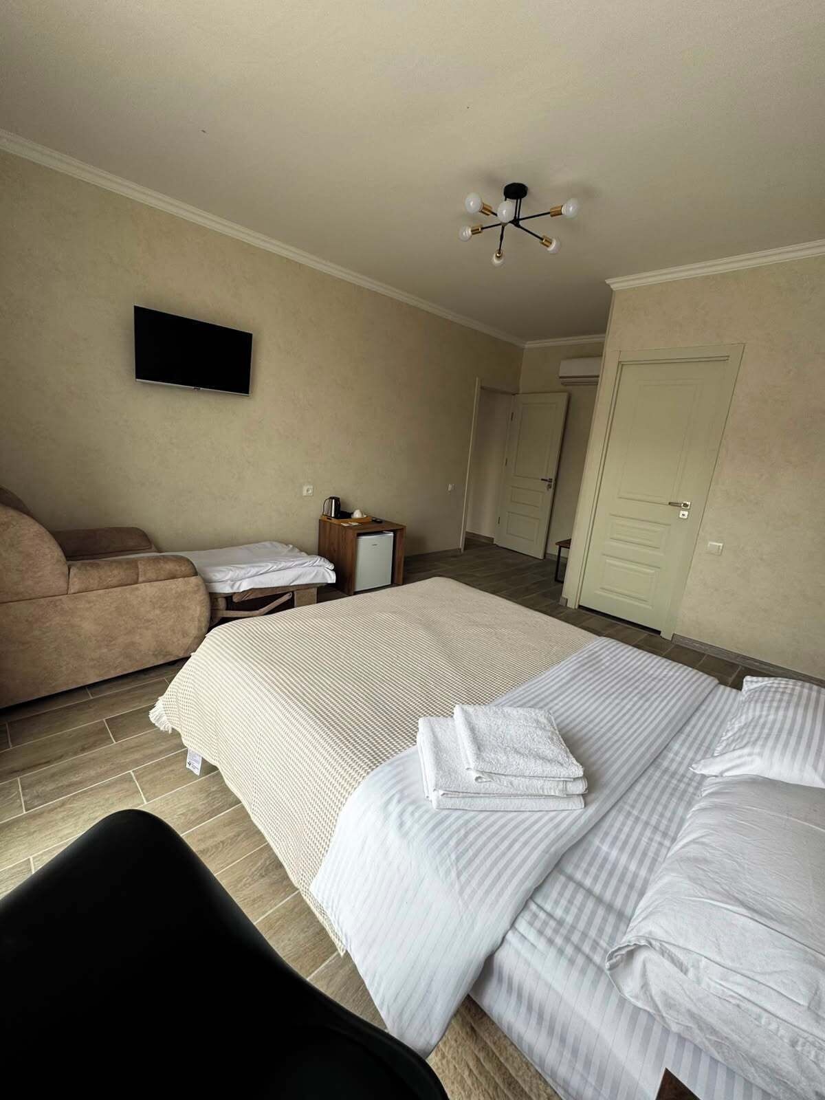 A hotel room with a bed, a sofa, a television, a small table with a coffee maker, and a door.