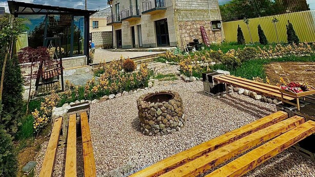 A modern house with a stone facade, a balcony, and a garden with a fire pit.