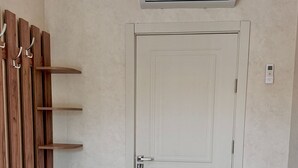 A room with a white door, a bench, a wall-mounted air conditioner, and a wall-mounted thermostat.